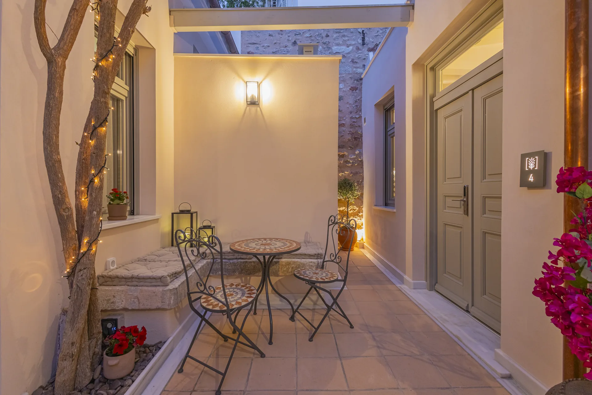 The courtyard entrance of Avlí & Phós at dusk, with a bistro table and bougainvillea