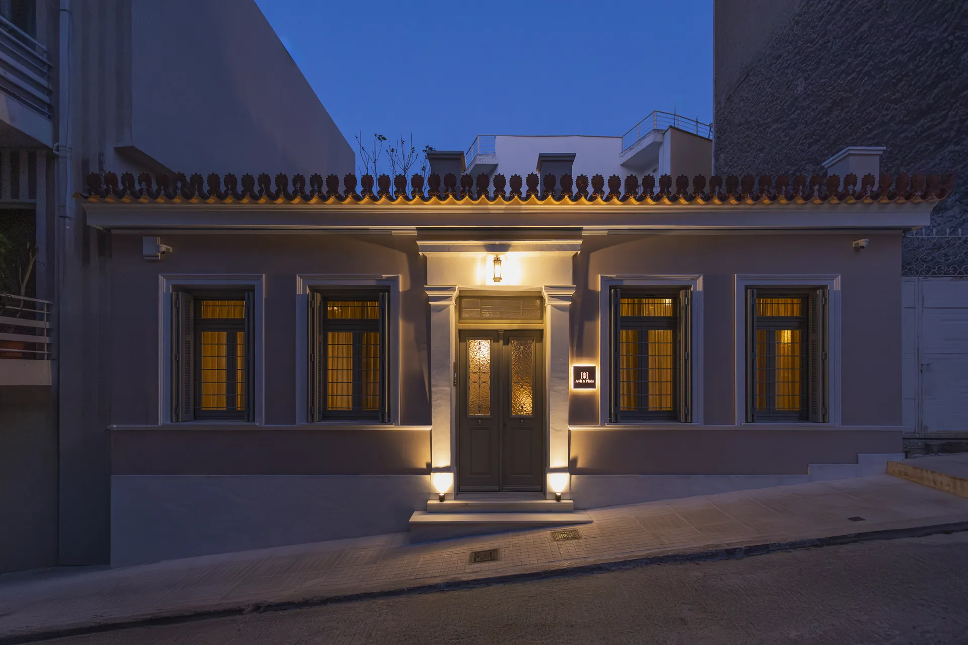 The restored neoclassical facade of Avlí & Phós at dusk in Thissio, Athens