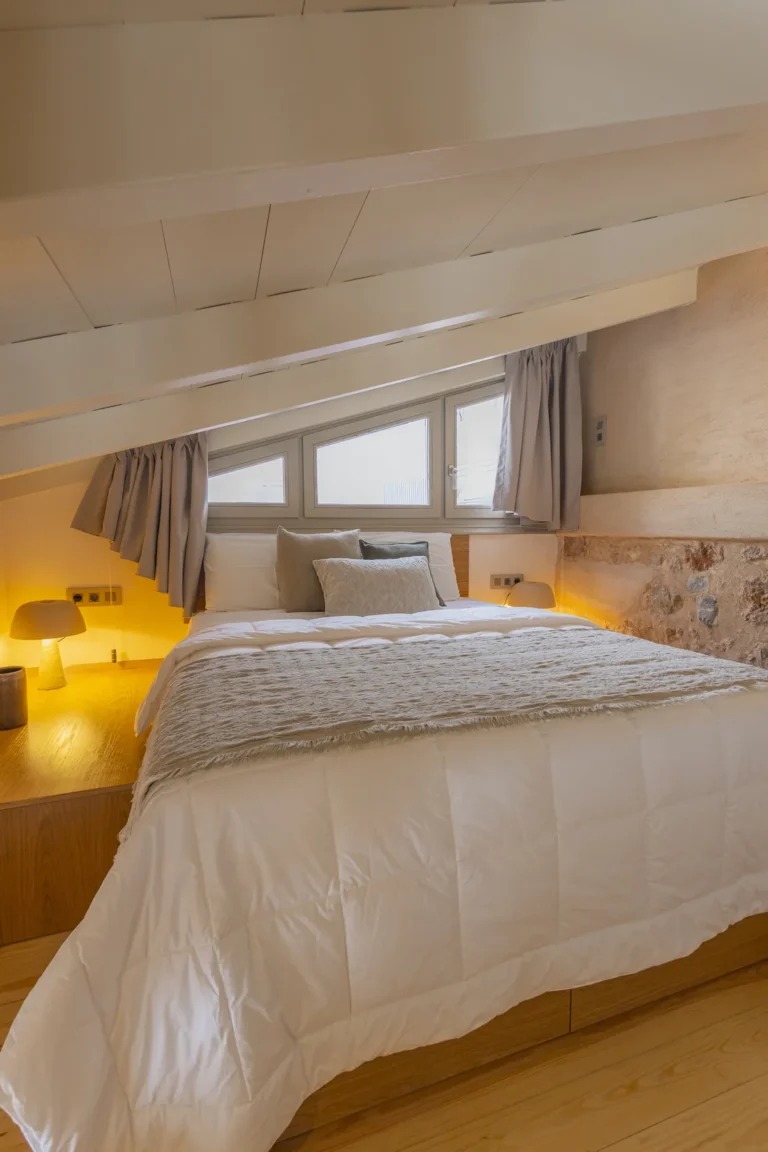 Loft bedroom of the Junior Suite with an exposed stone wall at Avlí & Phós